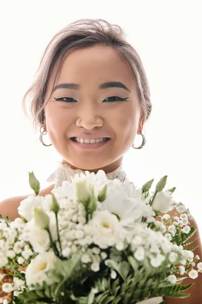 Portrait de mariée asiatique souriante avec maquillage grâce et bouquet de fleurs blanches sur fond clair — Photo de stock