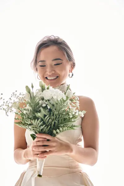 Happy asian young bride with grace makeup and bouquet of white flowers against light background — Stock Photo
