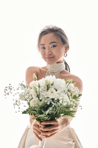 Attraente giovane donna asiatica con grazia trucco tenere fuori bouquet di fiori bianchi su sfondo chiaro — Foto stock