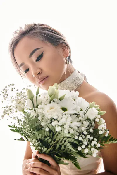 Encantadora mujer asiática en 20s viendo a blanco flores ramo en fondo claro - foto de stock