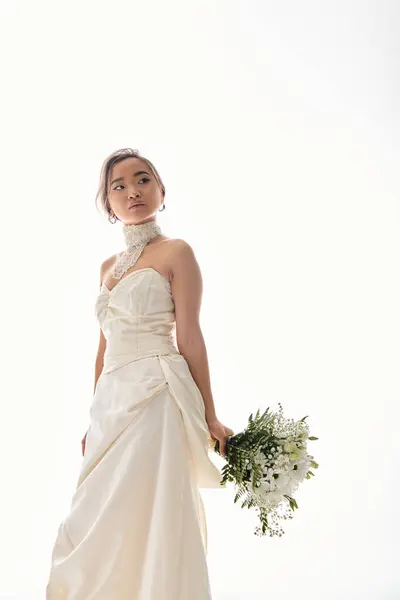 Attractive young asian woman in elegant white dress looking to side with bouquet of flowers — Stock Photo