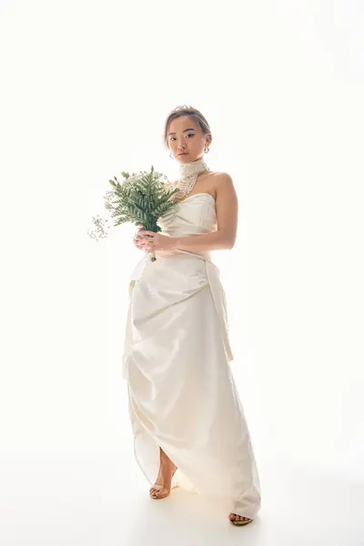 Sofisticación asiático joven mujer en blanco vestido posando a ramo de flores sobre fondo claro - foto de stock