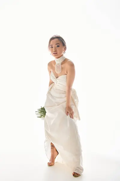 Elegante asiático joven mujer en elegante blanco vestido inclinado hacia adelante contra fondo claro - foto de stock