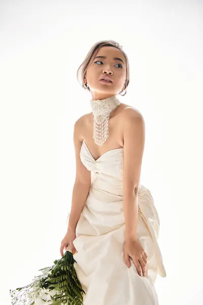 Чарівна азіатська жінка в білій сукні спирається вперед і дивиться на бік світлого фону — Stock Photo