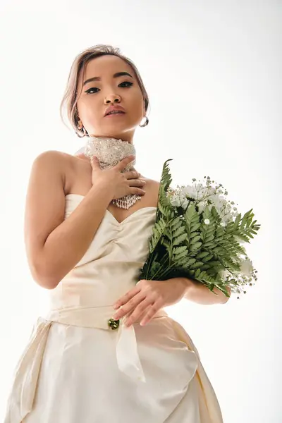 Alluring asian young bride in white necklace looking to camera with bouquet of flowers — Stock Photo