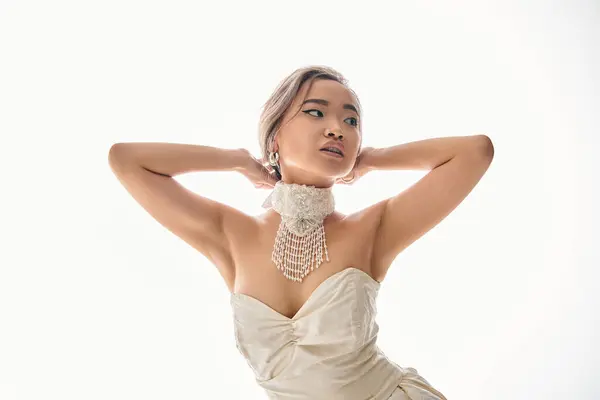 Витончена азіатська жінка в стильному намисті дивиться в бік і кладе руки за голову — стокове фото