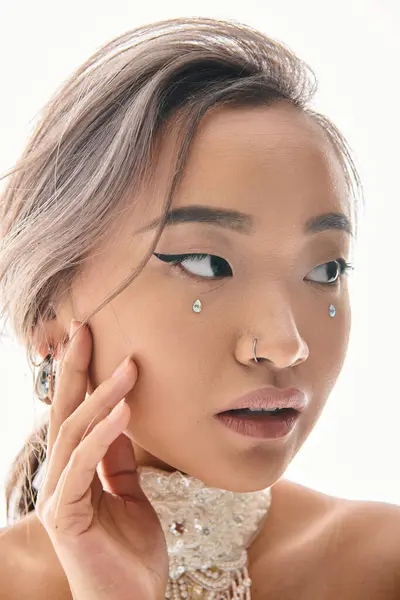 Крупним планом чарівна азіатська молода жінка з елегантним макіяжем дивиться в бік і торкається щоки рукою — стокове фото