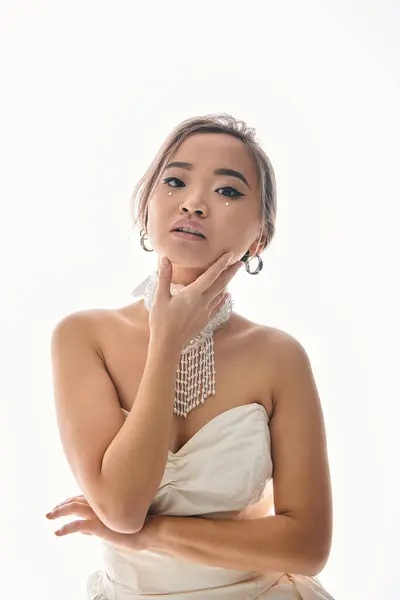 Элегантная азиатская молодая невеста в белом ожерелье нежное прикосновение к лицу с рукой на светлом фоне — стоковое фото