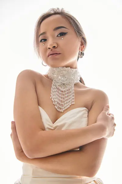 Belle asiatique femme en blanc grâce collier avec élégant maquillage étreinte elle-même sur fond clair — Photo de stock