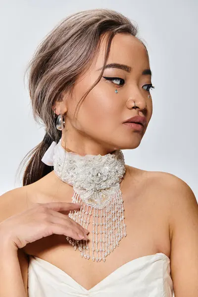 Изящная азиатская невеста в свои 20 лет нежно касается белого ожерелья на светлом фоне — стоковое фото