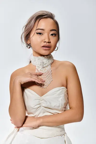 Элегантная азиатская невеста нежные прикосновения к белому ожерелью и глядя на камеру на светлом фоне — стоковое фото