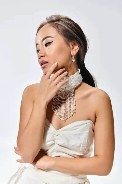 Elegante asiatische Braut in ihren 20er Jahren mit Anmut Make-up und Halskette zartes Posen auf hellem Hintergrund — Stockfoto