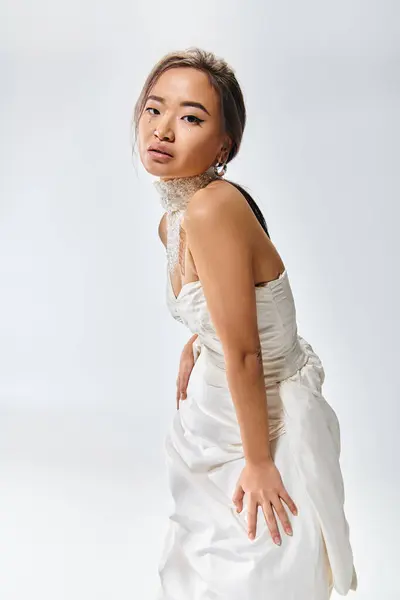 Graceful asian bride in elegant  white dress leaning forward against light background — Stock Photo