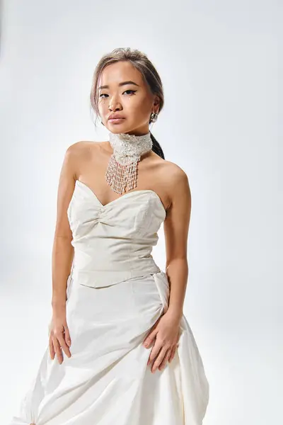 Atractivo asiático novia en blanco elegante vestido confiado posando contra luz fondo - foto de stock