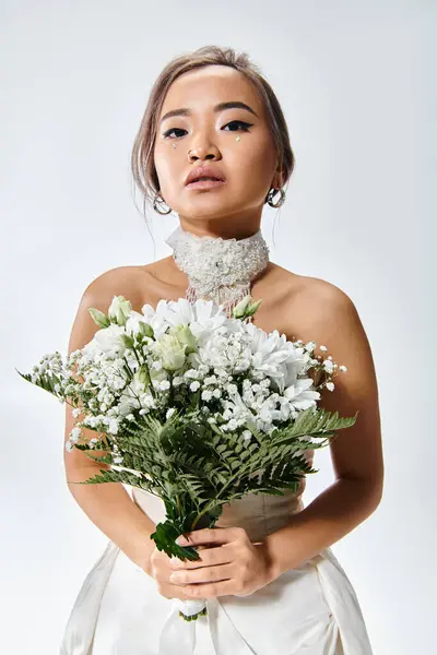 Graceful asian young bride in white elegant outfit with flowers bouquet on light background — Stock Photo