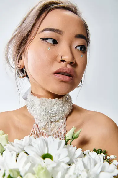 Очаровательная азиатская женщина в возрасте 20 лет с белыми цветами глядя в сторону на светлом фоне — стоковое фото