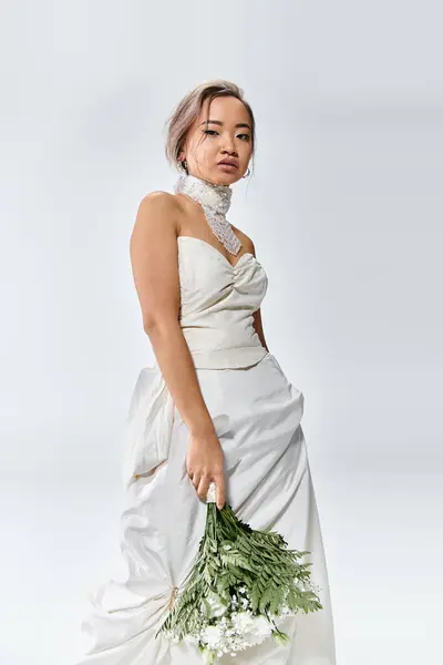 Charming asian young woman in white elegant outfit posing with flowers bouquet on light background — Stock Photo