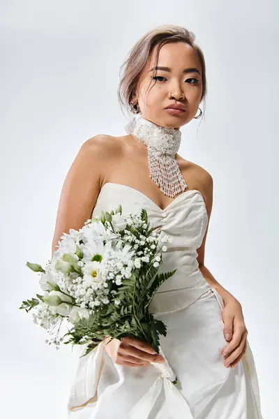 Asian young woman in white elegant outfit looking to camera and posing with flowers bouquet — Stock Photo