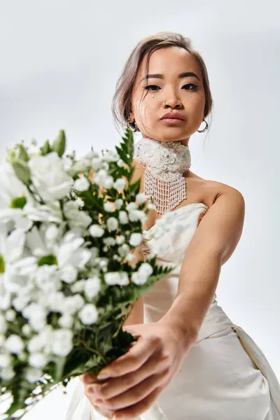 Affascinante donna asiatica nel suo 20s tenere fuori a fiori bianchi bouquet su sfondo chiaro — Foto stock