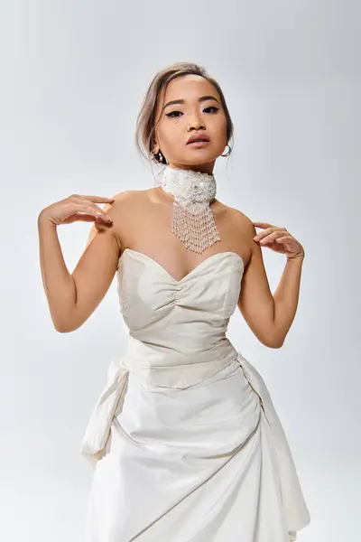 Elegante asiático joven mujer en blanco collar tocando a hombros con las manos sobre fondo claro - foto de stock