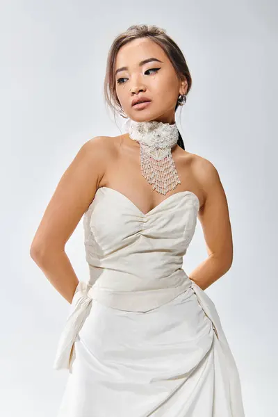 Elegante mujer joven en vestido elegante blanco posando con las manos detrás de la espalda sobre fondo claro - foto de stock