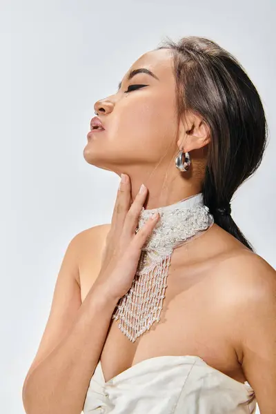 Profile of alluring young asian woman in 20s seductive touching to necklace against light background — Stock Photo