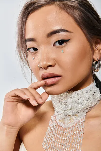 Atractivo asiático chica con elegante maquillaje buscando a cámara y tocando a los labios en la luz de fondo - foto de stock