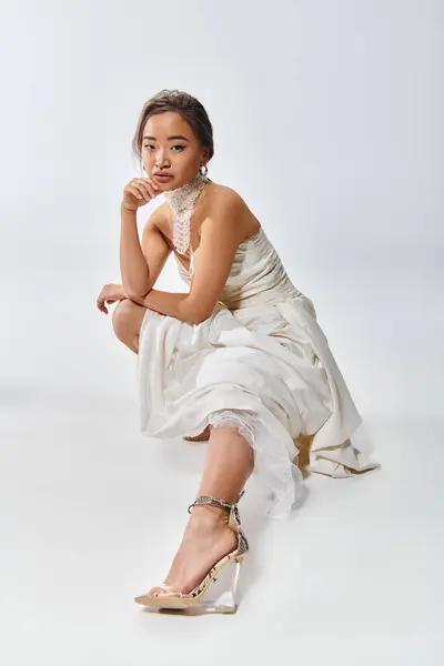 Atractivo asiático joven mujer en blanco elegante vestido agachado abajo y estirado pierna fuera en frente - foto de stock