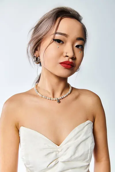 Atractiva mujer joven asiática con labios rojos y collar de perlas sobre fondo blanco - foto de stock