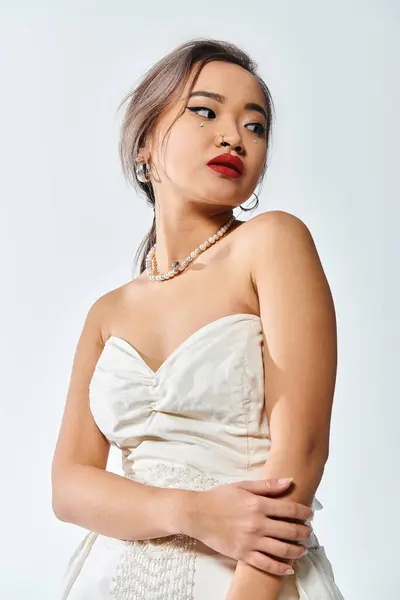 Заманчивая азиатская женщина в возрасте 20 лет с красными губами и жемчужным ожерельем смотреть в сторону на белом фоне — стоковое фото
