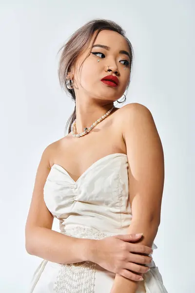 Alluring asian woman in her 20s with red lips and pearl necklace look to side on white background — Stock Photo