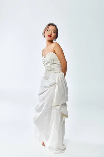 Bonita novia asiática con labios rojos y collar de perlas posando y mirando a un lado sobre fondo blanco - foto de stock