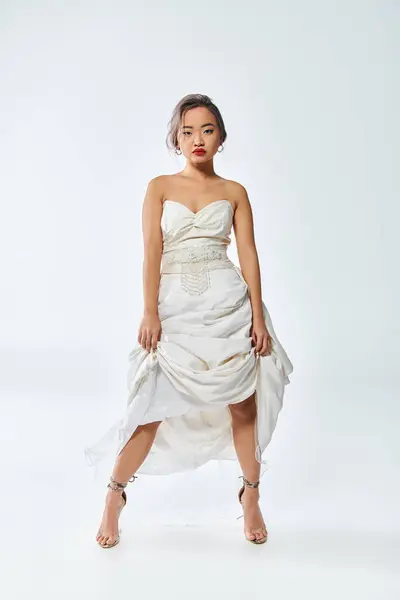 Asian woman in white elegant outfit with red lips lifted her dress on white background — Stock Photo