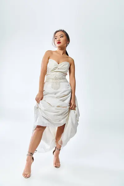 Attraente asiatico donna in bianco elegante vestito con rosso labbra sollevato il suo vestito e guardato a lato — Foto stock