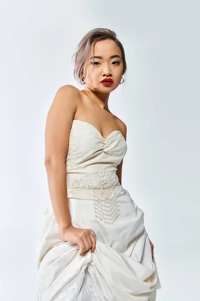Seguro asiático novia en blanco gracia traje con rojo labios levantó su vestido en blanco fondo - foto de stock