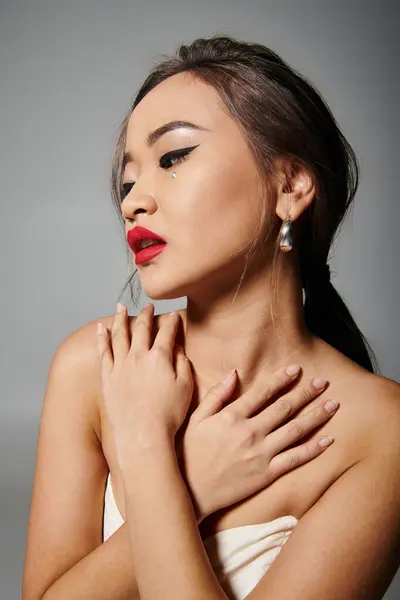 Atraente asiático jovem mulher com vermelho lábios cobertura para decote contra cinza fundo — Fotografia de Stock