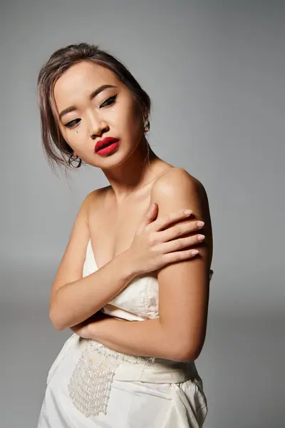 Retrato de mujer asiática en sus 20 años sosteniendo al hombro y mirando hacia atrás sobre fondo gris - foto de stock