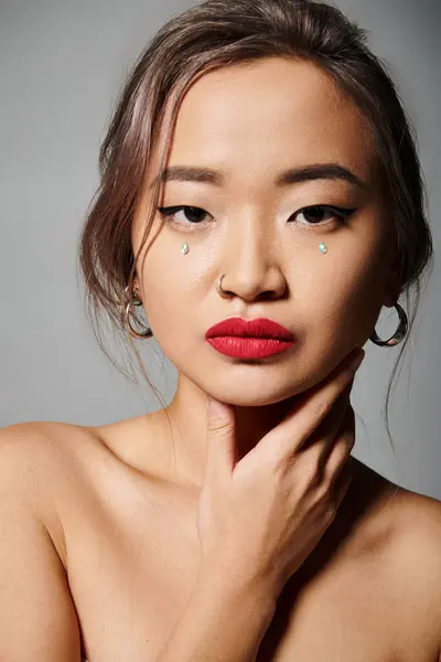 Портрет елегантної азіатської молодої жінки з червоними губами, що покривають шию рукою на сірому фоні — стокове фото