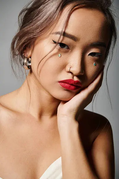 Porträt einer attraktiven asiatischen jungen Frau, die die Wange mit der Hand vor grauem Hintergrund bedeckt — Stockfoto