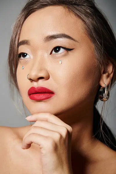 Nahaufnahme einer anmutigen asiatischen Frau mit elegantem Make-up, das bis zum Kinn reicht, vor grauem Hintergrund — Stockfoto