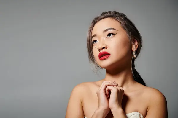 Attractive asian woman with red lips folding hands and looking to up against grey background — Stock Photo