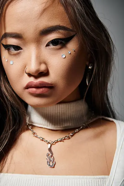 Schöne asiatische junge Frau in stilvollem Outfit mit gewagtem Make-up vor grauem Hintergrund — Stockfoto