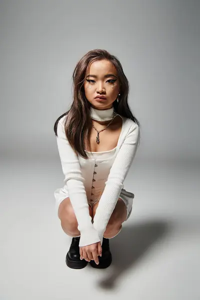Hübsche asiatische junge Mädchen in weißen stilvollen Outfit hockte sich vor grauem Hintergrund — Stockfoto