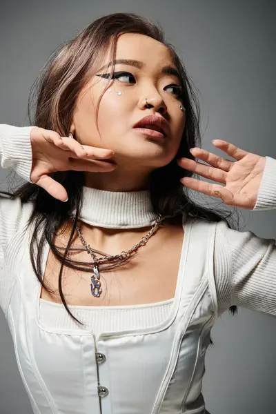 Retrato de encantadora mujer asiática con maquillaje pesado posando con las manos sobre fondo gris - foto de stock