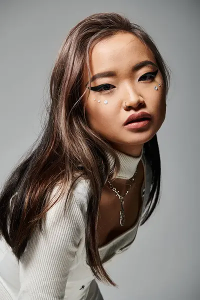 Atraente asiático mulher no 20s com pesado maquiagem lateral inclinado para a frente contra cinza fundo — Fotografia de Stock