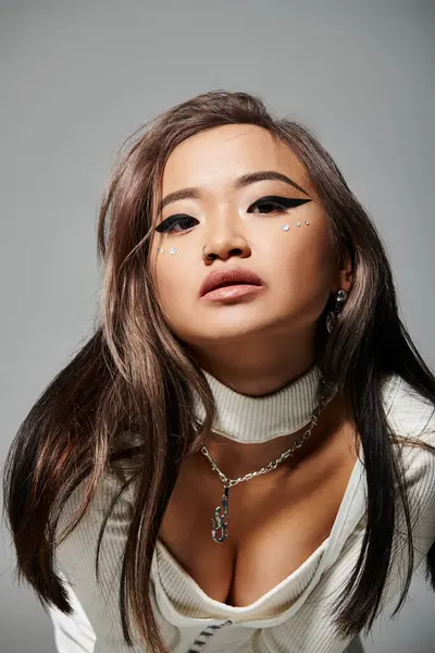 Encantador asiático jovem mulher com maquiagem pesada inclinando-se para a frente contra fundo cinza — Fotografia de Stock