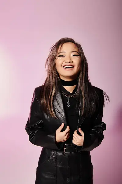 Lächelnde Asiatin im schwarzen Lederoutfit mit schwerem Make-up vor fliederfarbenem Hintergrund — Stockfoto