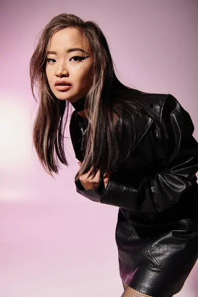 Hübsche Frau im schwarzen Leder-Outfit mit schwerem Make-up seitlich nach vorne gebeugt auf fliederfarbenem Hintergrund — Stockfoto