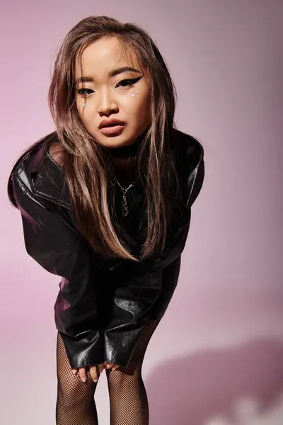 Asiatische junge Mädchen in schwarzem Leder-Outfit mit schwerem Make-up lehnt sich nach vorne auf fliederfarbenem Hintergrund — Stockfoto