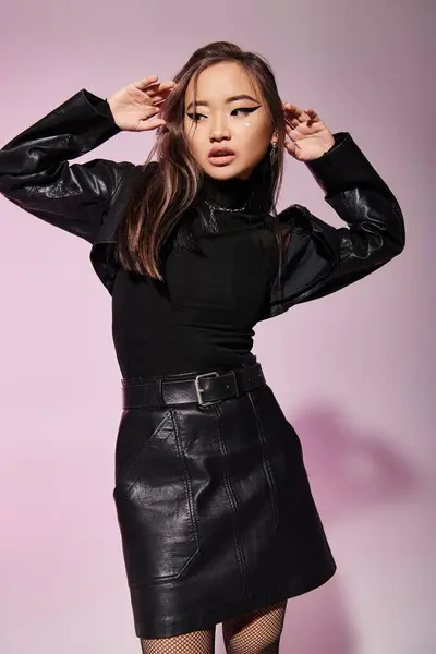 Linda asiático mulher no 20s no preto couro roupa segurar mãos ao redor para rosto no cinza fundo — Fotografia de Stock